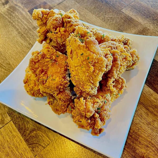 Crispy, golden-brown Korean fried chicken pieces, lightly sprinkled with herbs, on a white rectangular plate.