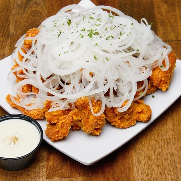 Dagiya's Korean fried chicken topped with thinly sliced white onions and parsley, with a side of white sauce.
