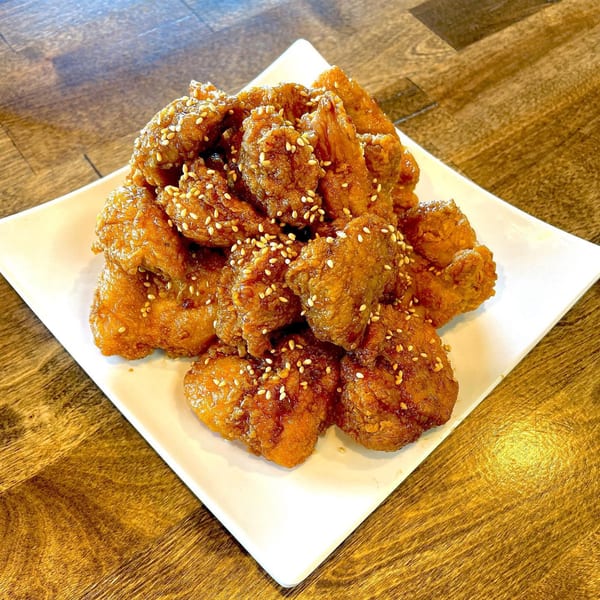 A white plate piled high with golden-brown Korean fried chicken pieces, sprinkled with sesame seeds.
